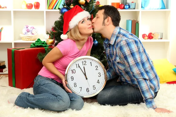 Jovem casal feliz segurando relógio perto da árvore de Natal em casa — Fotografia de Stock