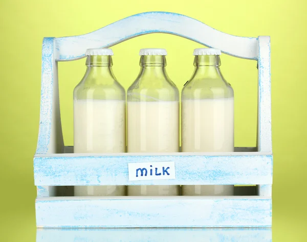 Milk in bottles in wooden box on green background — Stock Photo, Image