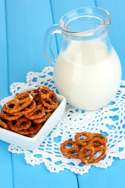 Tasty pretzels in white bowl and milk jug on wooden table close-up — Stock Photo, Image