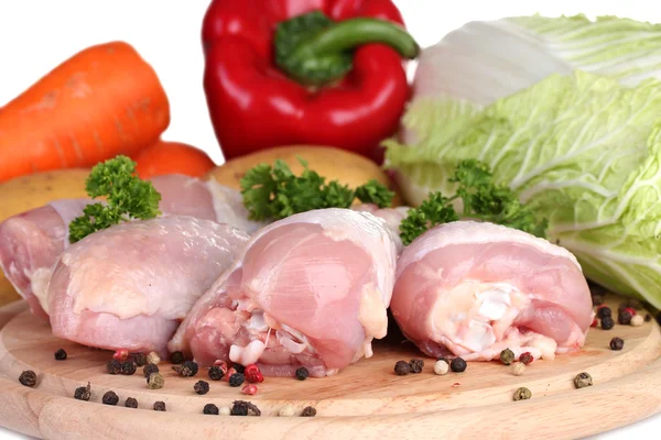 Fresh vegetables with raw chicken drumsticks and pork steak on cutting board isolated on white — Stock Photo, Image