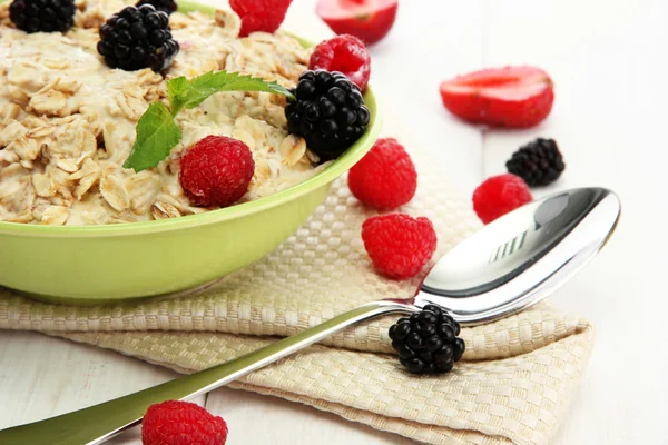 Tasty oatmeal with berries, on white wooden table — Stock Photo, Image