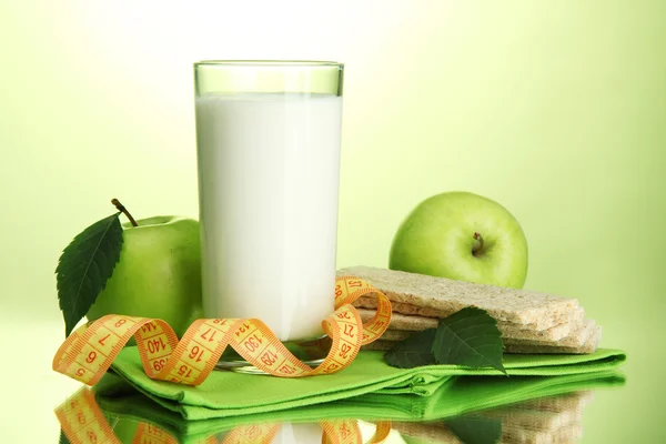 Vaso de kéfir, manzanas, panes fritos y cinta métrica, sobre fondo verde —  Fotos de Stock