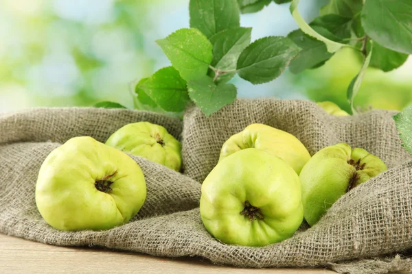 Sweet quinces with leaves, on burlap, on green background — Stock Photo, Image