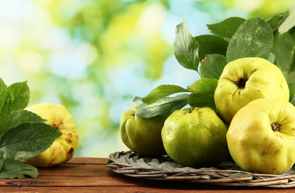 Sweet quinces with leaves, on wooden table, on green background — Stock Photo, Image