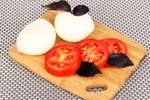 Sabrosa mozzarella con tomates en la tabla de cortar en la estera —  Fotos de Stock