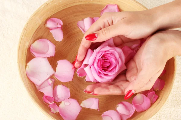 Manos de mujer con cuenco de madera de agua con pétalos — Foto de Stock