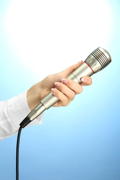 Main féminine avec microphone, sur fond bleu — Photo