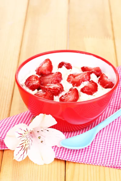 Hüttenkäse in roter Schüssel mit Erdbeeren in Scheiben auf Holztisch — Stockfoto