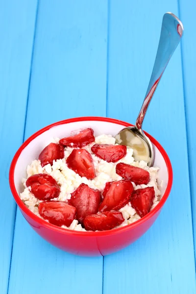 Cottage cheese in red bowl with sliced strawberries on blue wooden table — Stock Photo, Image