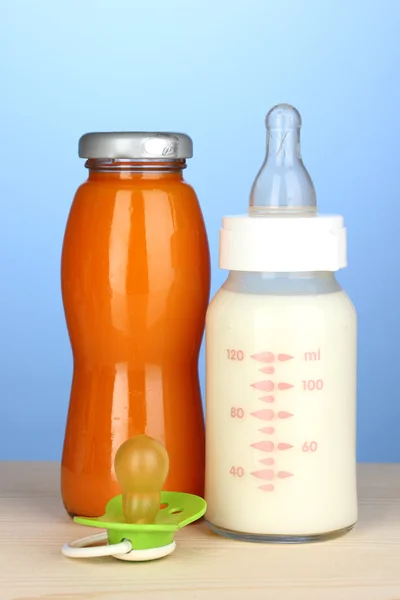 Bebê garrafa de leite e suco no fundo azul — Fotografia de Stock