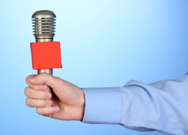 Erkek el ile mavi arka plan üzerinde mikrofon