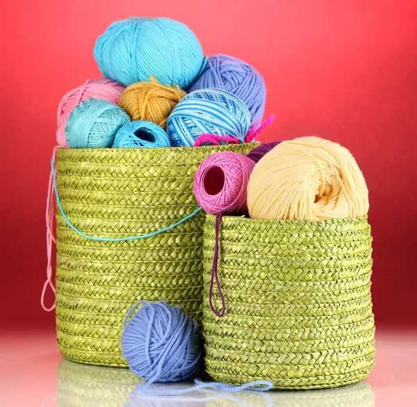 Красочная пряжа для вязания в зеленой корзине на красном фоне — стоковое фото