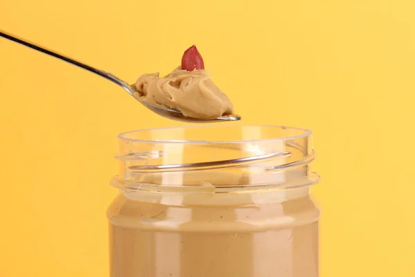 Delicious peanut butter in jar and spoon on yellow background — Stock Photo, Image