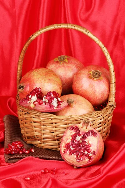 Ripe pomegranates on basket on red cloth background — Stock Photo, Image