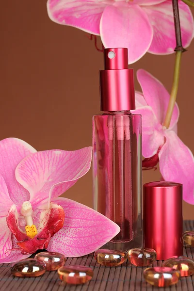 Women's perfume in beautiful bottle with orchids on brown background — Stock Photo, Image