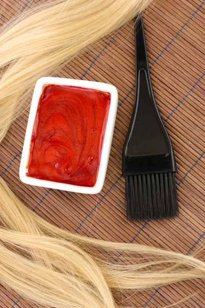 Hair dye in bowl and brush for hair coloring on brown bamboo mat, close-up Stock Image