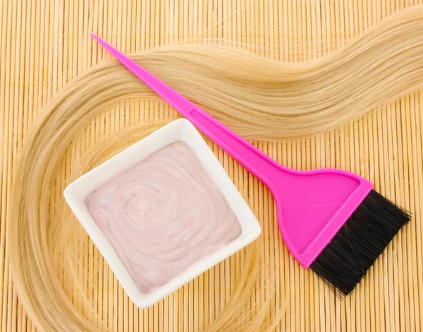 Tintura per capelli in ciotola e pennello per la colorazione dei capelli su tappetino di bambù beige, primo piano — Foto Stock