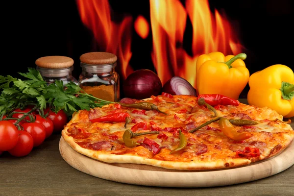 Smakelijke pepperoni pizza met groenten op houten bord op vlam achtergrond — Stockfoto