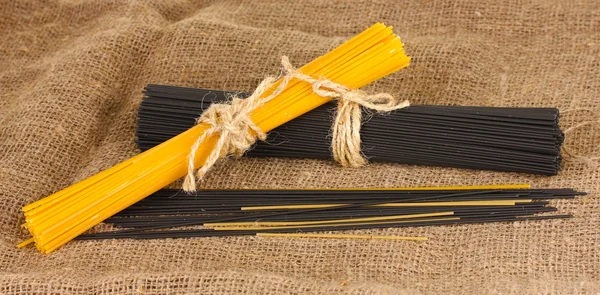 Black and yellow spaghetti on sackcloth background — Stock Photo, Image