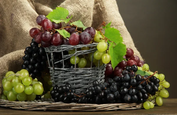 Assortment of ripe sweet grapes in basket, on grey background — Stock Photo, Image