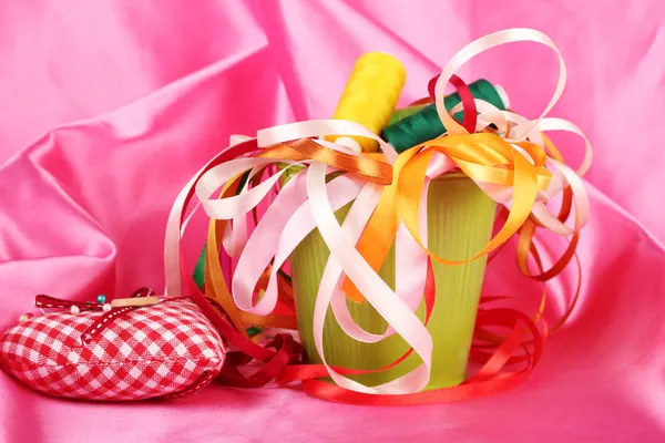 Color bucket with multicolor ribbons and thread on pink fabric background — Stock Photo, Image