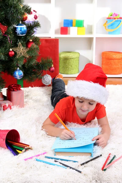 Kleine jongen in Kerstman hoed schrijft een brief aan de Kerstman — Stockfoto