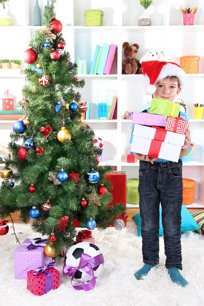 Little boy in Santa hat stands near Christmas tree with gifts Stock Image