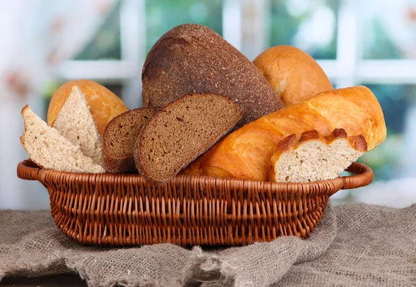 Fresh bread in basket on wooden table on window background — Stock Photo, Image