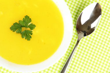 Yeşil masa örtüsü üzerinde beyaz tabak içinde kokulu çorba