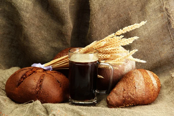 Tankard of kvass and rye breads with ears, on burlap background — Stock Photo, Image