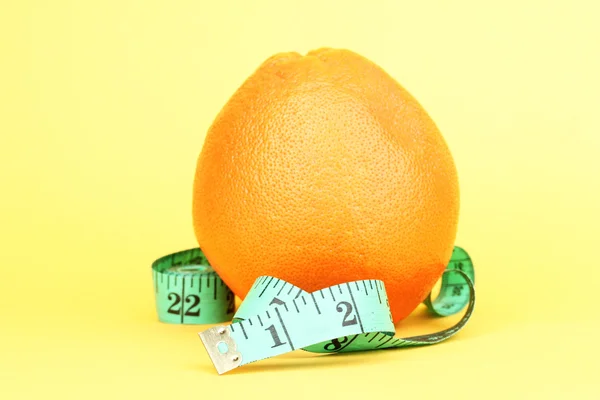 Orange with measuring tape on yellow background — Stock Photo, Image