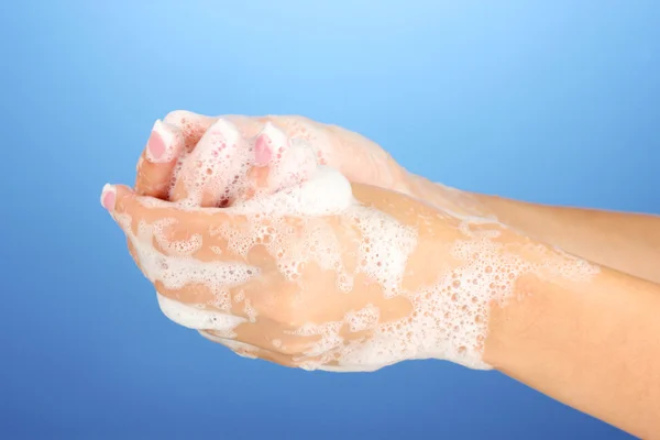 Les mains de la femme en savon, sur fond bleu gros plan — Photo