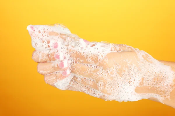 Woman's hands in soapsuds, on orange background close-up — Stock Photo, Image