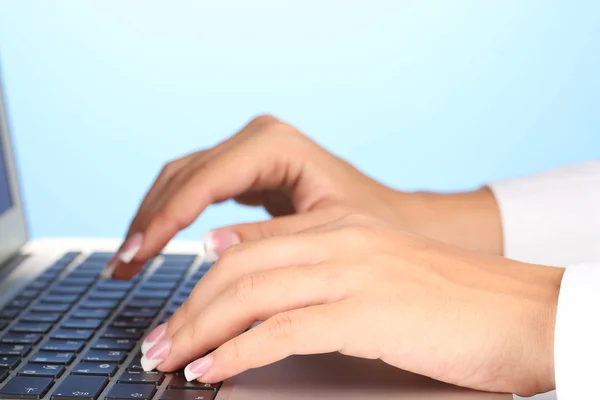 Руки, що друкуються на клавіатурі ноутбука крупним планом на синьому фоні — стокове фото