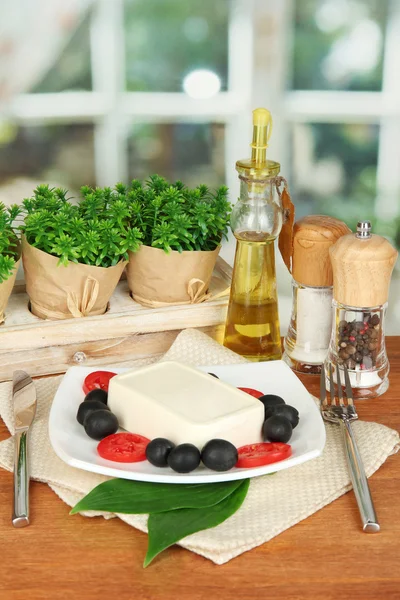 Feta-Käse auf Teller mit Gewürzen und Öl auf Holztisch auf Fensterhintergrund dekoriert — Stockfoto