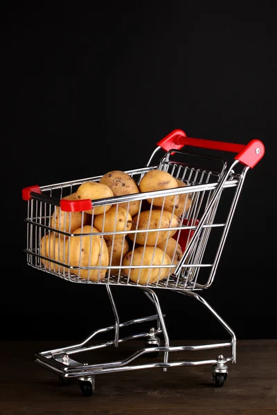 Ripe potatoes in trolley on wooden table on black background — Stock Photo, Image