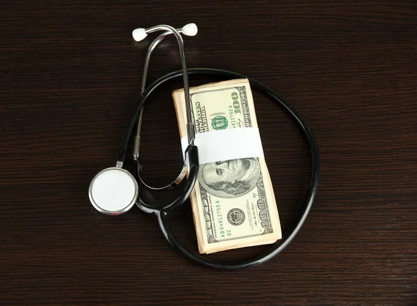 Healthcare cost concept: stethoscope and dollars on wooden background — Stock Photo, Image