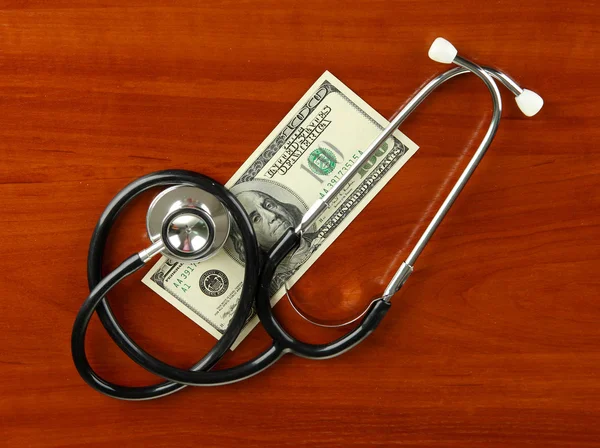 Healthcare cost concept: stethoscope and dollars on wooden background — Stock Photo, Image