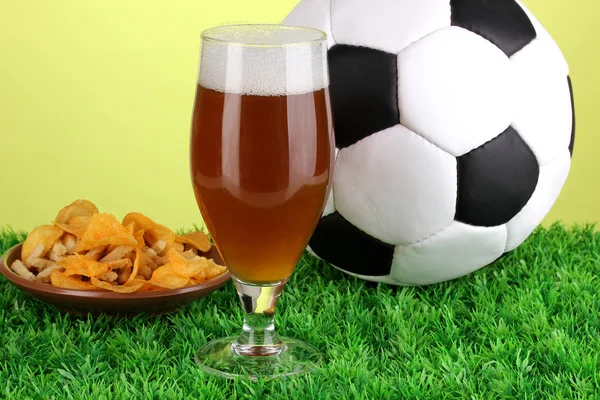 Sklenici piva s fotbalovým míčem na trávě na zeleném pozadí — Stock fotografie