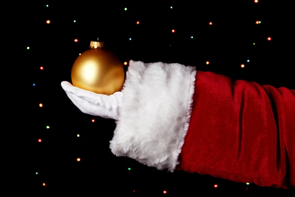Santa Claus mano celebración de la bola de Navidad sobre fondo brillante — Foto de Stock