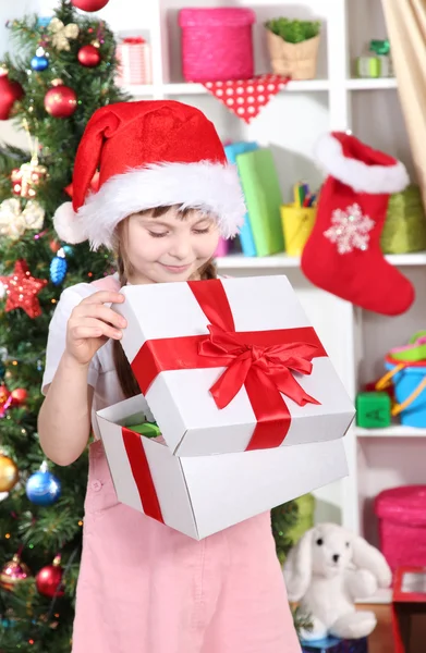 Ένα μικρό κορίτσι που ανοίγει ένα δώρο σε γιορτινή διακόσμηση δωμάτιο — Φωτογραφία Αρχείου