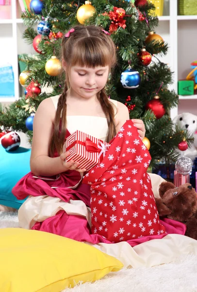 A little girl gets gifts from bag of Santa Claus in festively decorated room — Stock Photo, Image