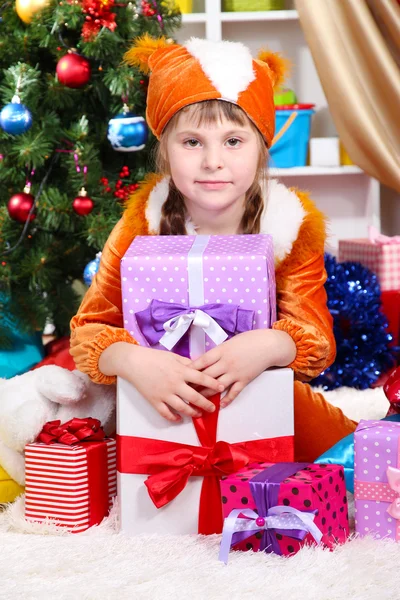 Little girl in suit of squirrels surrounded by gifts in festively decorated room — Stock Photo, Image