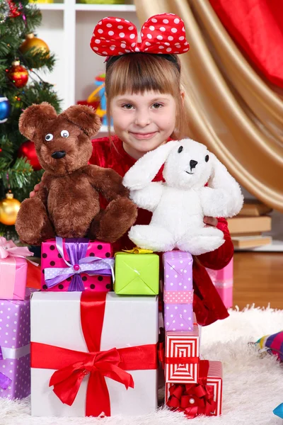 Hediyeler ve oyuncaklar festively bir şekilde dekore edilmiş oda çevrili Kırmızı elbiseli güzel küçük bir kız — Stok fotoğraf