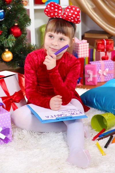 Menina bonita em vestido vermelho escreve carta ao Papai Noel em quarto festivamente decorado — Fotografia de Stock