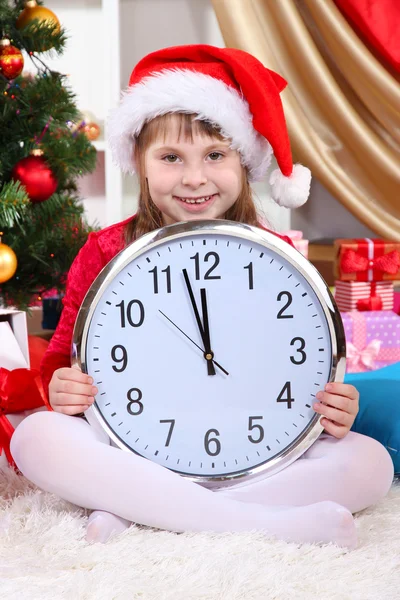 Hermosa niña con reloj en anticipación de Año Nuevo en la habitación festivamente decorada — Foto de Stock