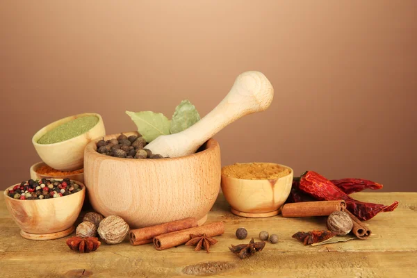 Mortar, bowls and spoons with spices, on table on brown background — Stock Photo, Image