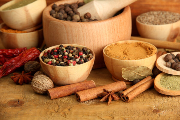 mortar, bowls and spoons with spices, on wooden background