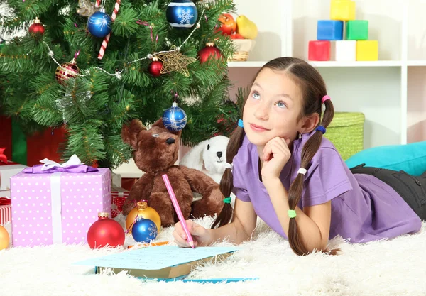 Kleines Mädchen schreibt Brief an Weihnachtsmann in der Nähe des Weihnachtsbaums — Stockfoto