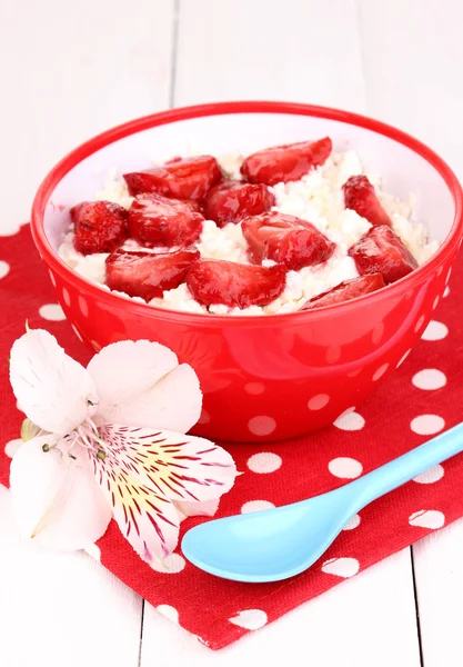 Hüttenkäse in roter Schüssel mit Erdbeerscheiben auf weißem Holztisch — Stockfoto